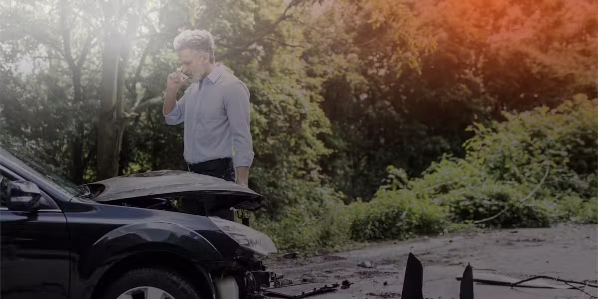 edited image of a man on the phone looking at his busted car following an accident